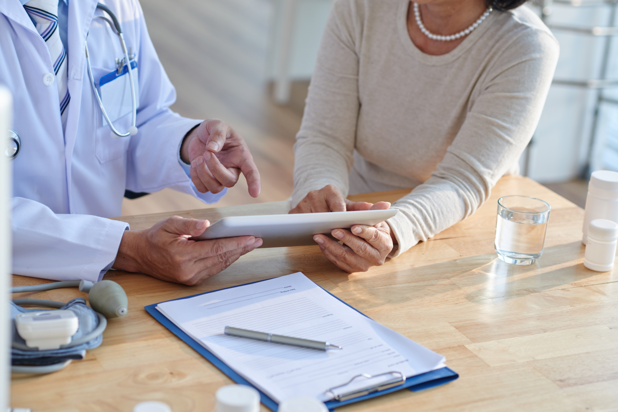 Close-up shot of unrecognizable doctor using digital tablet and discussing records with female patient